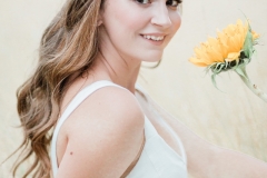 A bride in a field, wearing natural makeup and her hair in soft waves. 