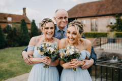Two bridesmaids with their Dad, wearing blue dresses, natural makeup and boho wedding hairstyles. 